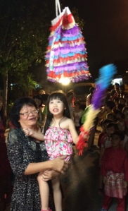 Grandma raising her little granddaughter up to hit the piñata in the game